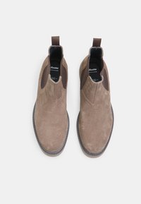 Botine din suede maro, cu panouri laterale elastice și bucle de prindere. Textură netedă și vârf rotunjit cu cusături contrastante în jurul tălpii.