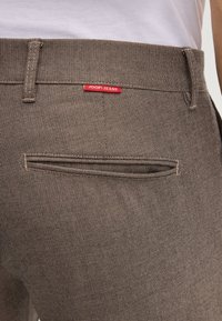 Pantaloni marroni dallo stile texturizzato con una tasca posteriore che presenta un'etichetta rossa "JOOP JEANS". Filo dritto con passanti per la cintura e una finitura pulita.