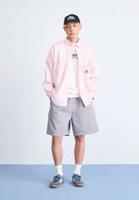 Lys rosa skjorte med knapper, hvit t-skjorte med logo, stripete shorts. Blå joggesko med hvite detaljer, svart caps. Enkel, uformell urban antrekk.