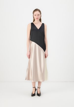 A sleeveless dress with a black top and a beige, asymmetrical hem. Made of smooth fabric, it features a V-neck and falls to mid-calf.