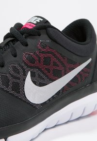 Zapatilla deportiva negra con parte superior de malla que presenta un patrón rojo y gris. Incluye un swoosh blanco de Nike y una suela texturizada con acentos en rosa.