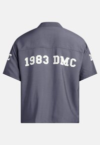 Siva majica kratkih rukava s velikim bijelim ispisanim tekstom "1983 DMC" na leđima. Širok kroj s ravnim rubom.