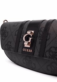 Borsa Guess nera con esterno texturizzato, chiusura con logo distintivo e dettagli in pelle a strisce. Design compatto e curvo, con dettagli sofisticati.