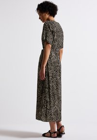Maxikleid mit Leopardenmuster, kurzen Ärmeln, lockerer Passform und glattem Stoff. Kombiniert mit schwarzen Sandalen mit Knöchelriemen und einem kleinen Absatz.
