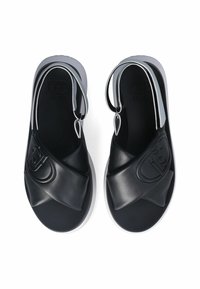 Black slide sandals made of soft leather with a crisscross strap design, featuring a logo detail and a white rubber sole.