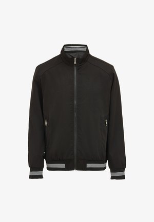 Musta pommikankaan takki, jossa on vetoketjukiinnitys edessä, sivutaskut, ribbaatut hihansuut ja helma, valkoisilla raidoilla, sekä pystykaulus. Sujuva kankaan pinta.