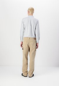 Hellblau gestreiftes Hemd mit Button-Down-Kragen, kombiniert mit beigen Cargo-Hosen mit mehreren Taschen und schwarzem Schuhwerk.