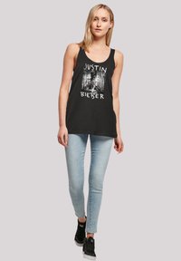 Schwarzes Tanktop mit einem Grafikdruck, auf dem "Justin Bieber" steht, kombiniert mit hellblauen Skinny Jeans und schwarzen Turnschuhen.