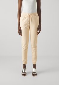 Pfirsichfarbene Jogginghose mit elastischem Bund und Kordelzug. Glattes Material, schmal zulaufende Form, mit Bündchen an den Knöcheln, kombiniert mit metallic-farbenen Rutschen-Sandalen.