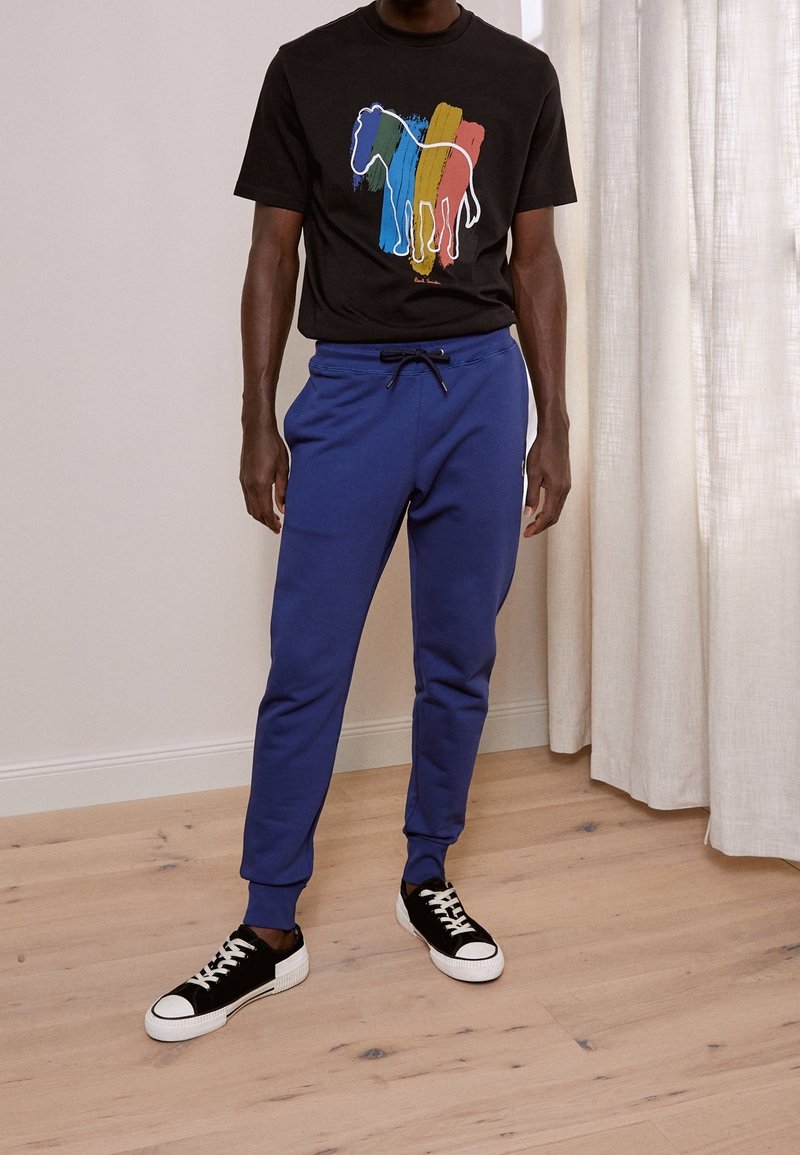 Black t-shirt with colorful horse graphic, paired with blue sweatpants featuring a drawstring waist. Black and white sneakers complete the outfit.