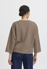 Felpa marrone a vestibilità ampia con scollatura rotonda e maniche a tre quarti, abbinata a jeans blu scuro, vista da dietro.