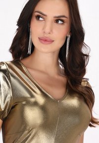 Metalen gouden jurk met een gladde textuur, V-hals en korte puffmouwen. Bevat kristal hangoorbellen voor extra detail.
