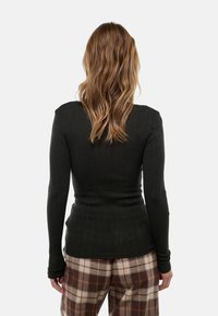 Haut à manches longues côtelé vert foncé avec une silhouette ajustée et des détails de tissu texturé, associé à un pantalon à carreaux marron et beige.