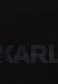 Materiale nero testurizzato con un logo "KARL" prominente e leggermente in rilievo, che presenta la silhouette di una figura sul lato sinistro.