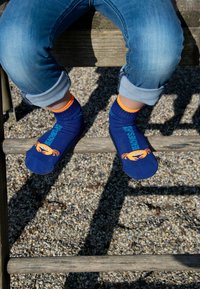 Marineblaue Socken mit einem orangefarbenen Krebsdesign und dem Text "Beach Day", mit kontrastierenden orangen Bündchen, getragen mit hochgekrempelten Jeanshosen.