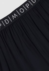 Ceinture élastique noire avec texte en logo gris clair ; texture de tissu doux et froncé. Design simple et minimaliste sans accents ni motifs supplémentaires.