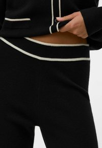 Ensemble en deux pièces en maille noire avec un accent crème. Le pull présente une poche et un bouton ; le pantalon a une taille rayée assortie.