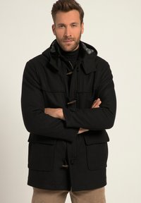 Abrigo negro hecho de tela gruesa con capucha, cierre de toggles y dos bolsillos frontales. El forro interior presenta un estampado de cuadros.