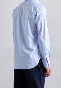 Camicia a scacchi blu chiaro, con polsini abbottonati, orlo curvo, tessuto misto cotone, texture liscia, vista posteriore con pantaloni scuri.