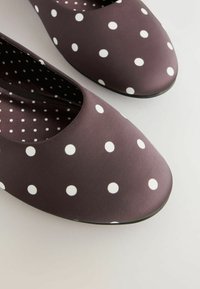 Braune Ballerinas mit glatter Oberfläche, außen mit großen weißen Punkten und einem gemusterten Innenfutter in ähnlichem Farbschema.