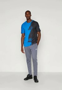 Blå och svart mönstrad t-shirt med kort ärm i kombination med grå mjukisbyxor som har vita sidostreck och svarta sportskor.