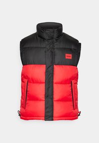 Doudoune sans manches avec col montant, partie supérieure noire, partie inférieure rouge, fermeture éclair devant, poches latérales zippées et étiquette rouge "HUGO" sur la poitrine.