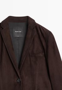 Brown suede blazer with a notched collar, single button closure, and chest pocket. Lined interior with brand label. Smooth texture.