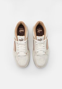 Vita och beige sneakers i mocka och läder. Har perforerat tåskt, snörning och logotypdetaljer på tungan och sidan.