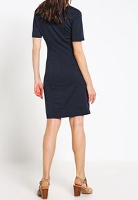 Robe bleu marine à manches courtes avec une silhouette ajustée. Caractérisée par une texture élégante et une coupe longueur genou, associée à des talons beiges.