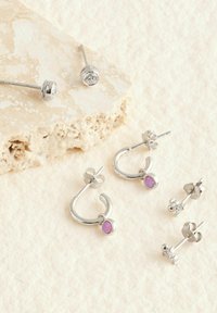 Pendientes de plata que incluyen un par de aros con una piedra púrpura y un conjunto de pendientes de botón con diseños circulares y florales.