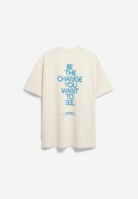 Roomwit oversized t-shirt met blauwe tekst op de achterkant: "WEES DE VERANDERING DIE JE WILT ZIEN." Inclusief een merklogo onderaan.