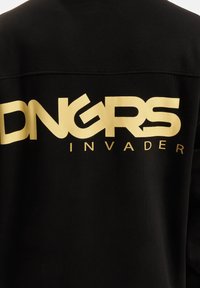 Fekete pulóver, amelynek hátulján nagy arany "DNGRS INVADER" felirat található. Az anyag lágy és sima tapintású, ami a hétköznapi viseletre jellemző.