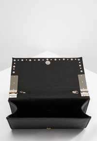 Sac à main en cuir noir avec des clous en argent le long du bord supérieur, comportant un fermoir métallique et un espace intérieur ouvert pour le rangement.