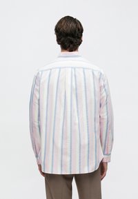 Ελαφρύ πουκάμισο με μακριά μανίκια, με κάθετες ρίγες σε ροζ, ανοιχτό μπλε και λευκό. Κλασικός γιακάς και μανσέτες με κουμπιά. Λεπτομέρεια πιέτας στο πίσω μέρος.