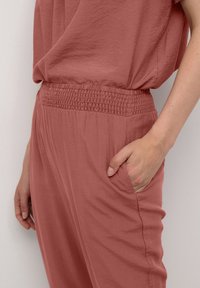 Roze outfit gemaakt van lichtgewicht stof, met een relaxte pasvorm, textuur in de taille en zijzakken. Glad, licht gekreukt textuur.
