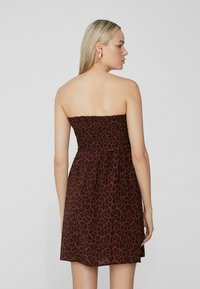 Robe brune sans bretelles avec un motif léopard, un buste smocké texturé et une jupe évasée, vue de dos.