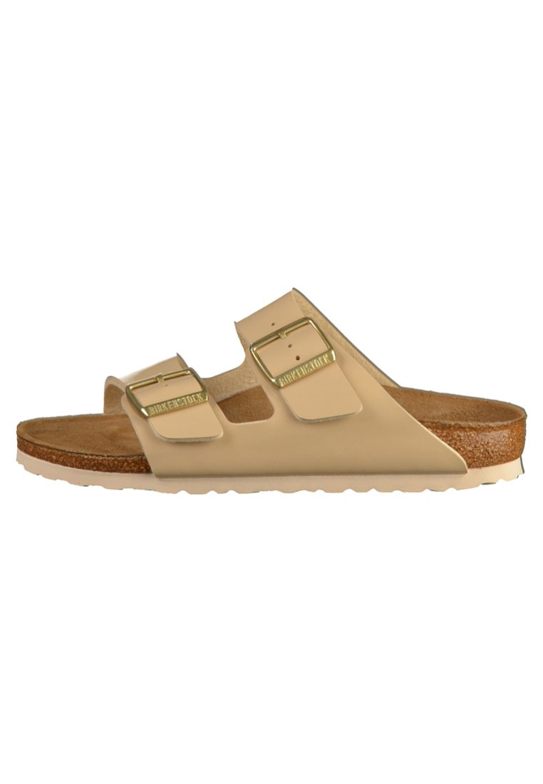 Sandalo slide beige con due cinturini regolabili, fibbie dorate e una soletta in sughero marrone. Suola in gomma per grip e durata.