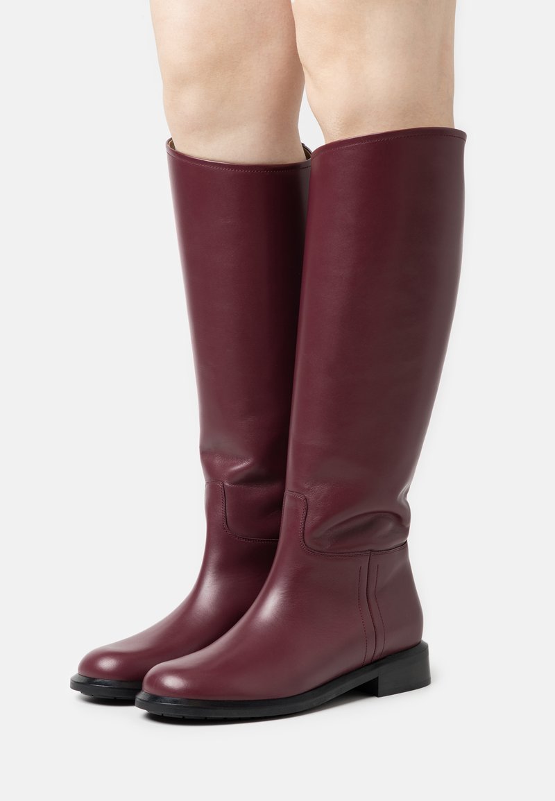 Knöchelhohe bordeauxfarbene Lederstiefel mit einer glatten Oberfläche, runder Zehenform, minimalistischen Design und flacher schwarzer Gummisohle.