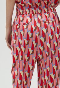 Colorful patterned trousers with a red, blue, and brown abstract design. Features elastic waistband and two back pockets. Smooth fabric texture.