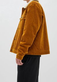 Giubbotto in velluto a coste di colore giallo senape, con un morbido colletto bianco, chiusura frontale con bottoni e tasche laterali. Tessuto texturizzato con motivo a righe.
