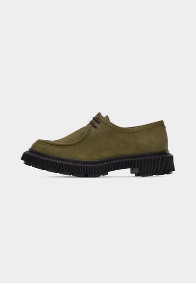 Chaussure à lacets en daim vert olive avec semelle noire épaisse à rainures, petit talon et bout arrondi, vue de côté sur un fond blanc.