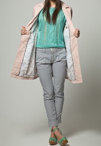 Ljust rosa trenchcoat med blommig foder, turkosstickad tröja, randiga byxor och gröna sandaletter med rem om vristen.