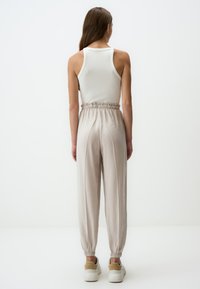 Lichtbeige joggerbroeken met elastische tailleband en taps toelopende enkels. Gecombineerd met een witte geribde tanktop, ontworpen voor een losse fit. Soepele textuur.