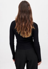 Black ribbed long-sleeve top with a fitted design, featuring a waistband and smooth texture, paired with tailored black pants.