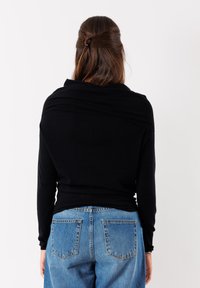 Top nero a maniche lunghe con design drappeggiato e dettagli a coste, abbinato a jeans in denim blu a vita alta con due tasche posteriori.