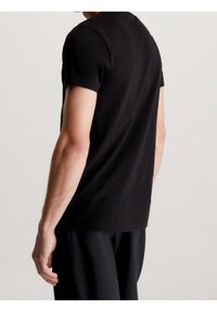 Musta lyhythihainen t-paita, valmistettu puuvillasta. Siinä on pyöreä pääntie ja rento istuvuus, esitetty takakulmasta, jossa näkyvät hartian ja käsivarren yksityiskohdat.