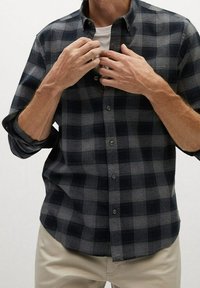 Chemise à carreaux boutonnée en gris foncé et bleu marine, fabriquée en tissu doux. Dotée d'un col et de manches longues retroussées aux poignets.
