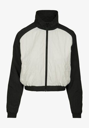 Lühendatud jakk, millel on must-valge värvipalett, valmistatud siledast ja kergest kangast, kõrge krae ja elastne vöökoht.