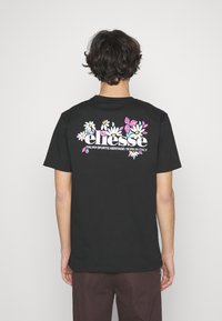 Sort bomulds t-shirt med et farverigt blomstermotiv og logoet "ellesse" på ryggen. Korte ærmer og rund halsudskæring.