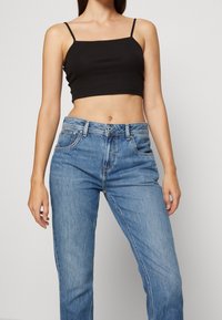 Top corto negro sin mangas con tirantes finos, combinado con jeans rectos de color azul claro que cuentan con bolsillos frontales y cierre de botón.